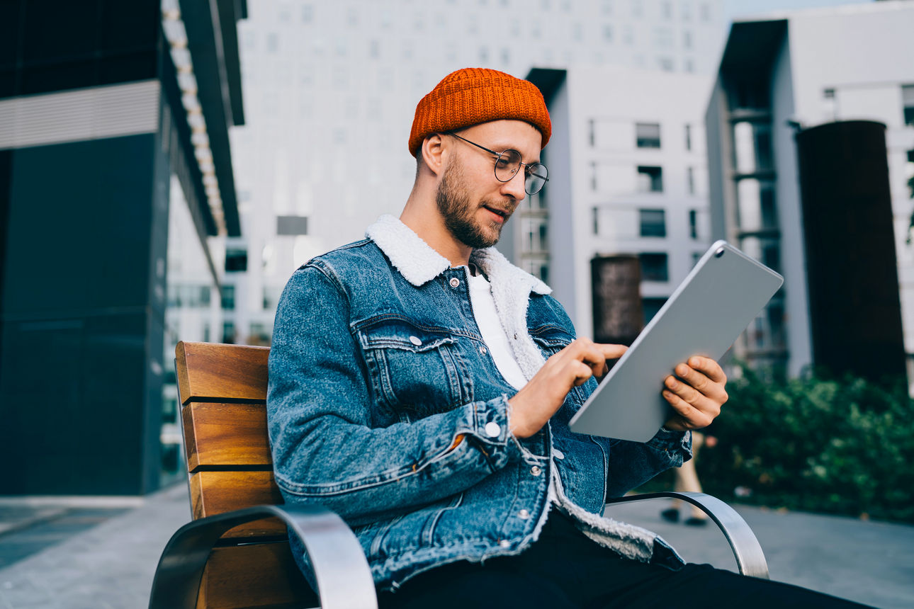 Mann mit einem Tablet in der Hand auf einer Bank im Freien