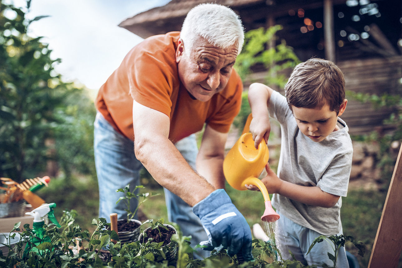 Großvater und Enkel spielen im Garten mit Gartengeräten.