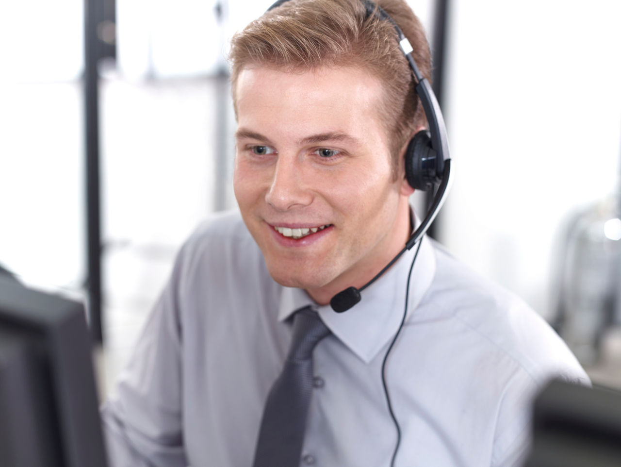 Mann sitzt lächelnd am Schreibtisch und telefoniert mit einem Headset