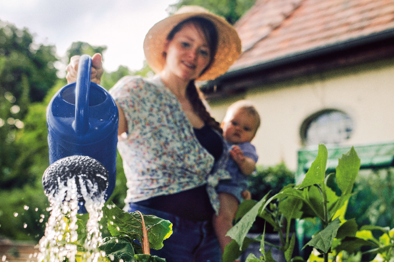 Eine Frau mit Baby auf dem Arm gießt Pflanzen