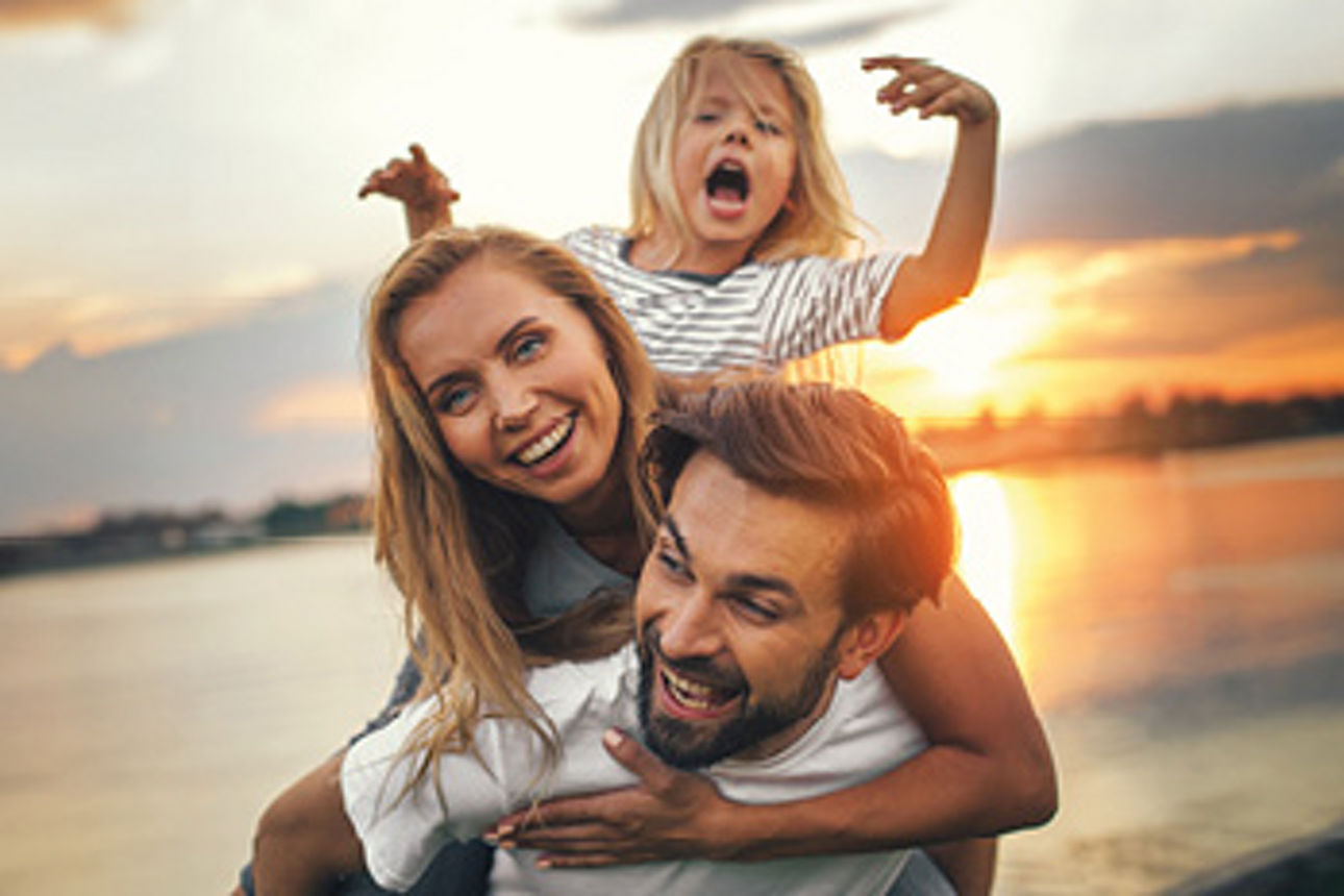Ein junge Famile steht vor dem Sonnenuntergang an einem See