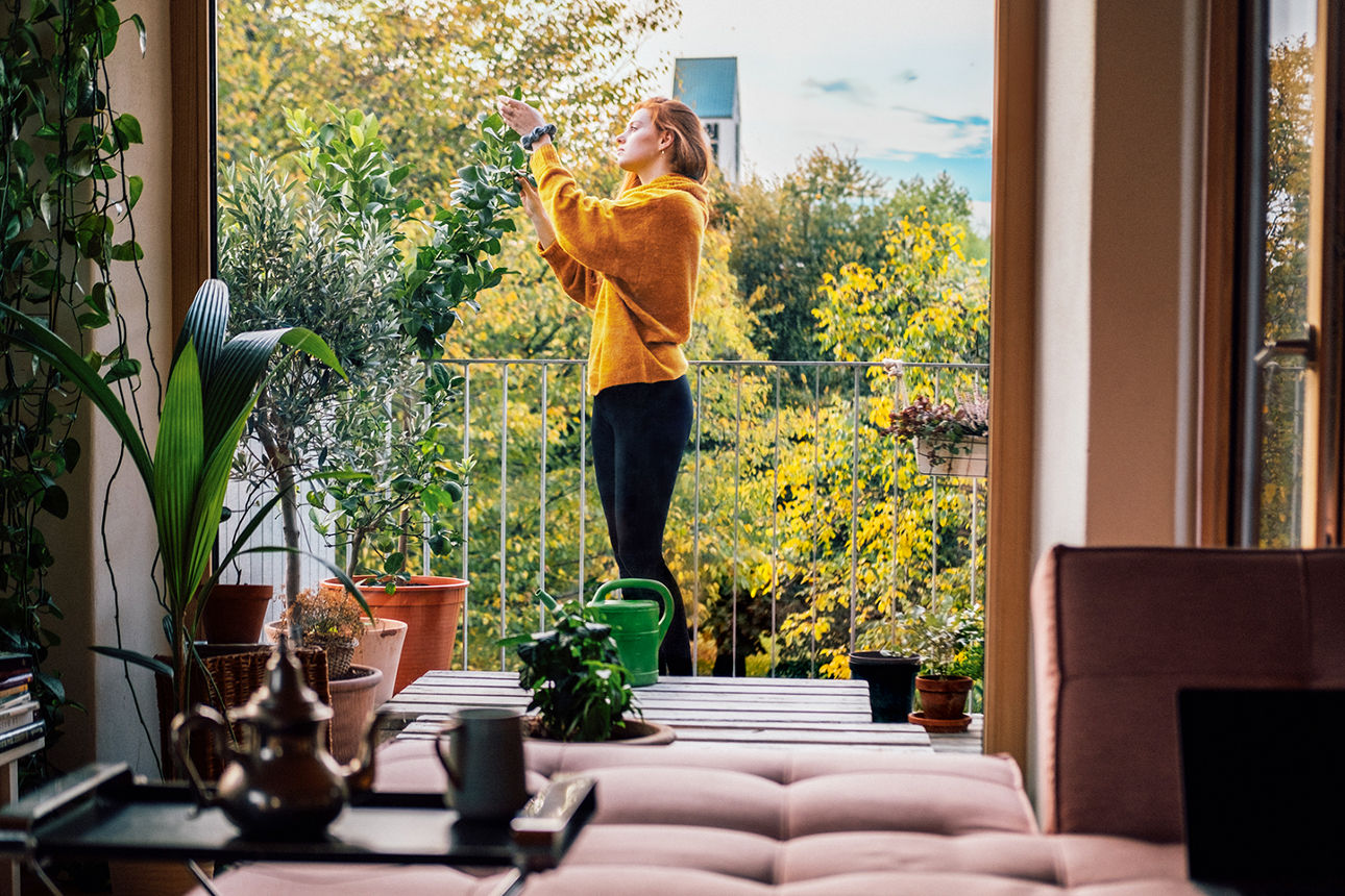 Junge Frau steht auf dem Balkon und kümmert sich um die Pflanzen