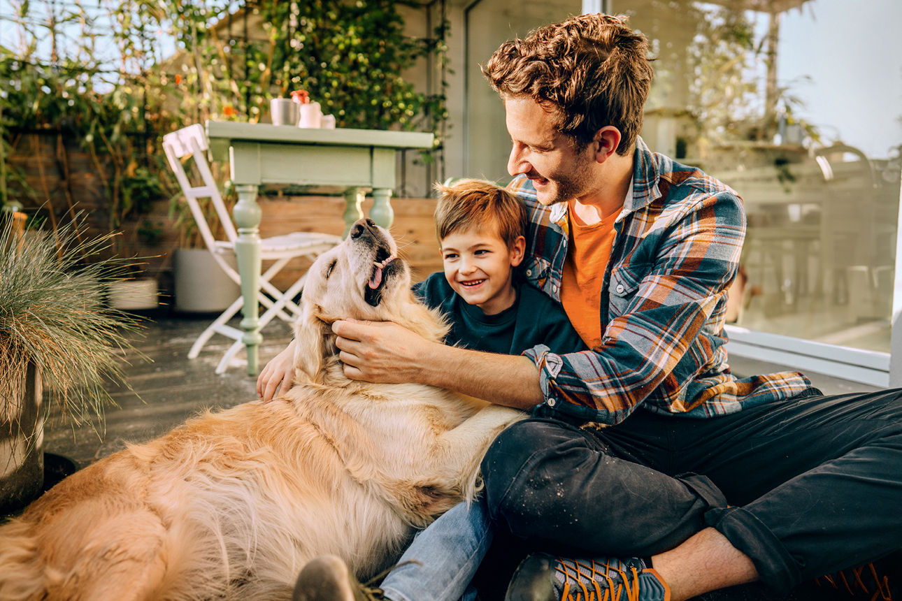 Ein Mann sitzt mit einem Kind aud dem Boden und beide steicheln dabei einen Hund.