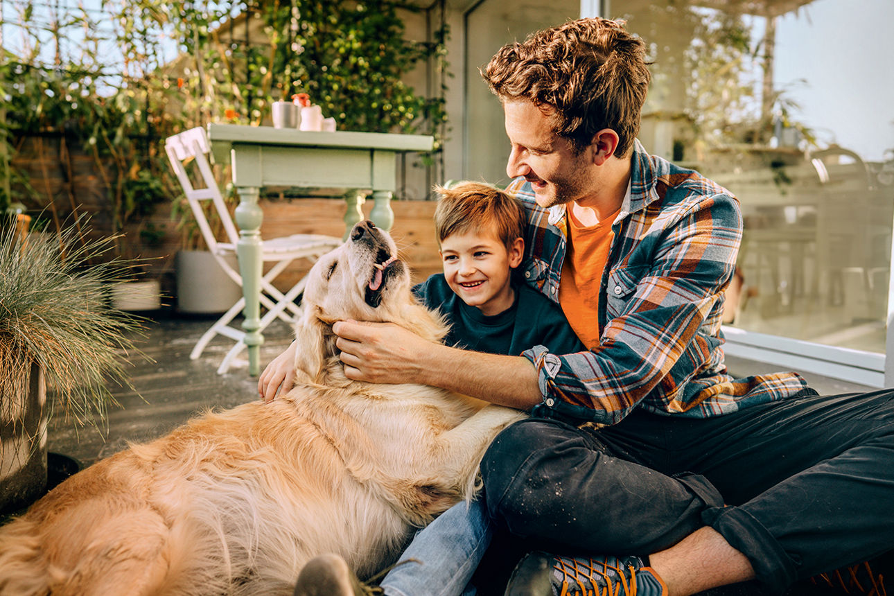 Foto von Vater, Sohn und ihrem Haustier, wie sie gemeinsam auf dem Balkon ihres Loft-Apartments Zeit genießen.