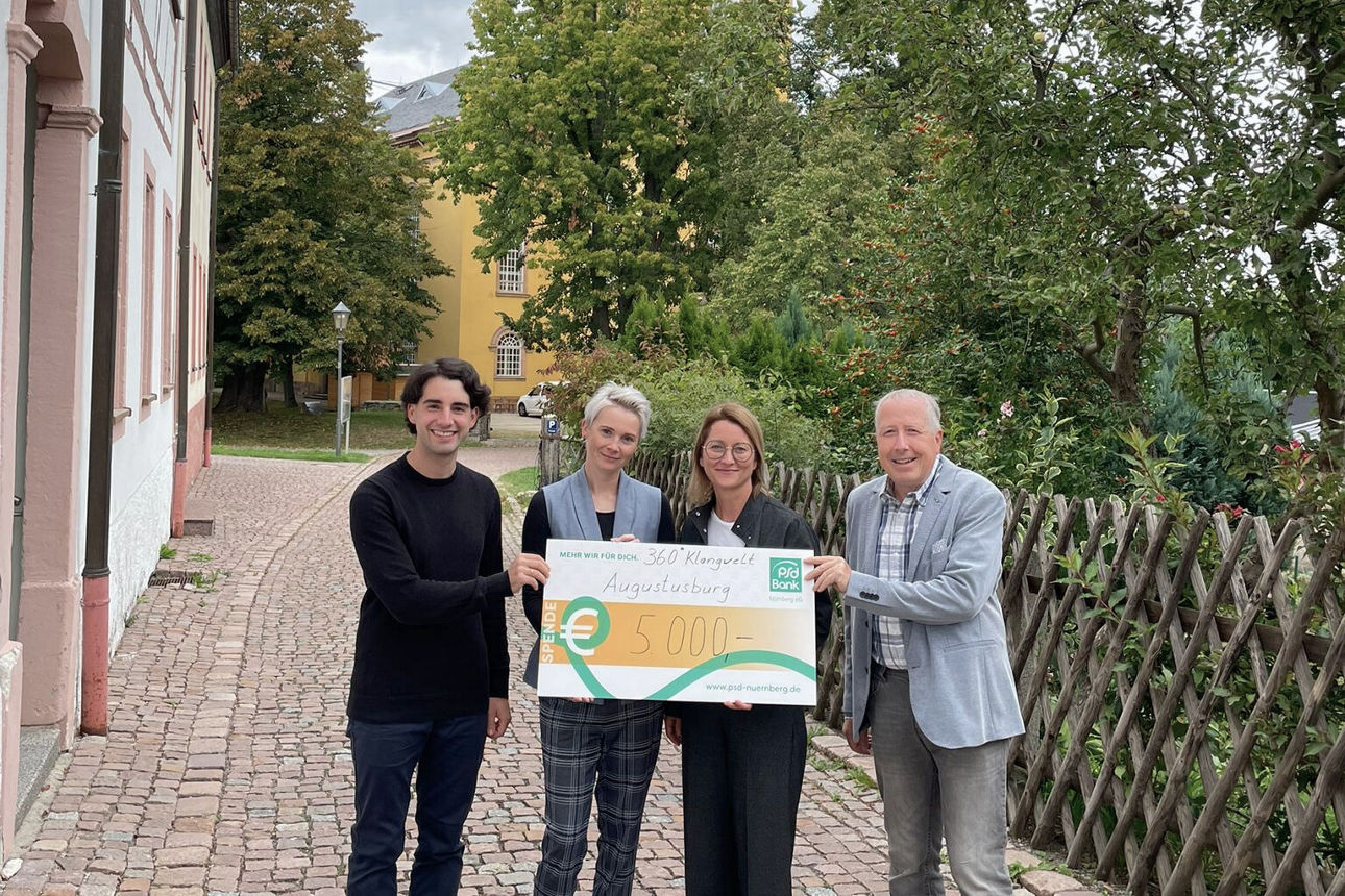 Ein Kollege der PSD Bank Nürnberg übergibt einen Spendencheck  an 360° Klangwelt Augustusburg
