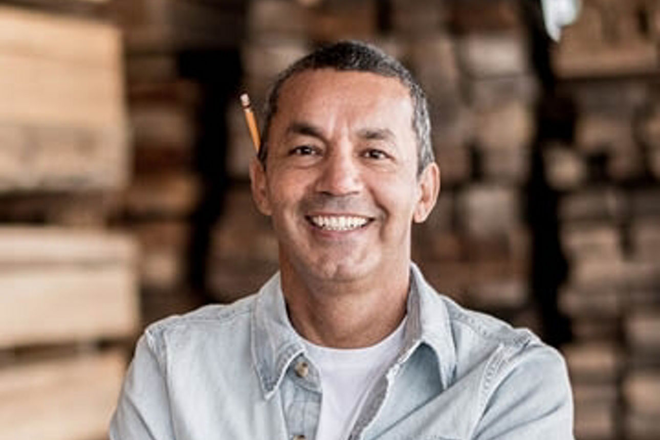 Ein Mann in einer Jeansjacke steht vor einem großen Holzstapel