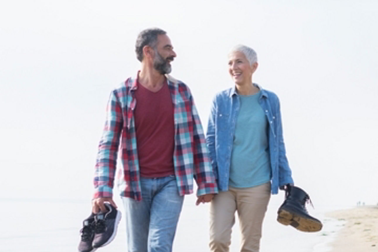 Glückliches älteres Paar geht Hand in Hand am Strand entlang