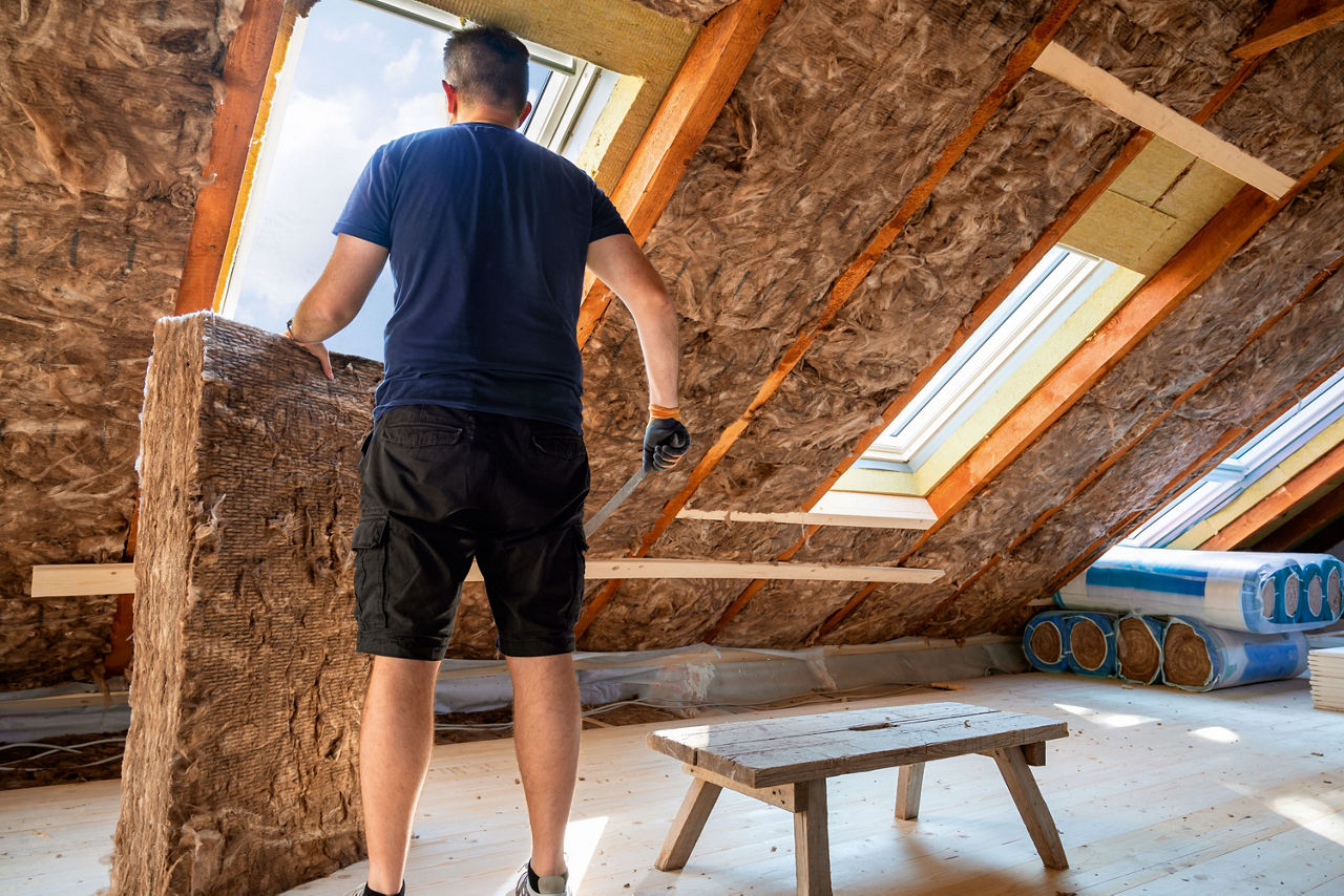 Mann bringt Dachdämmung an für energetische Sanierung