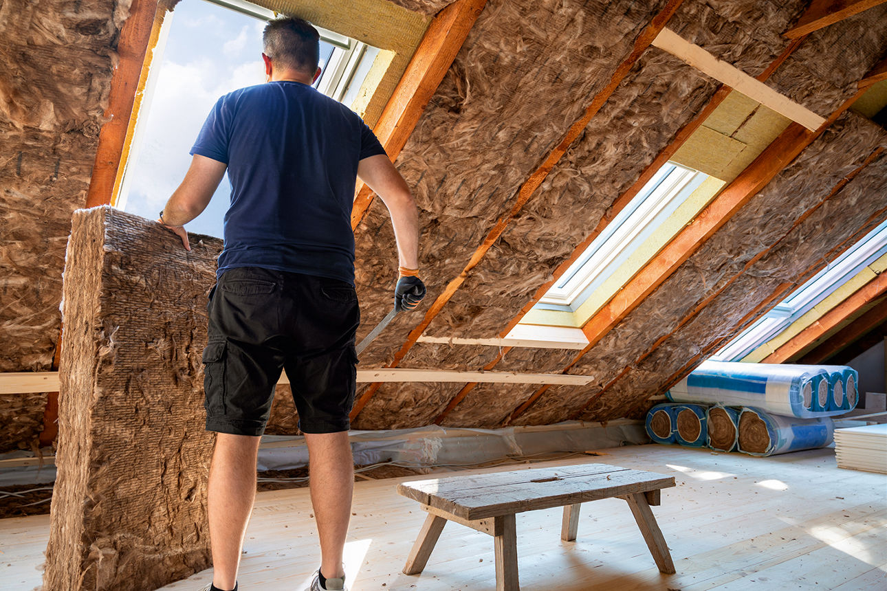Handwerker schneidet Dämmmaterial zur Dämmung des Dachbodens zu.