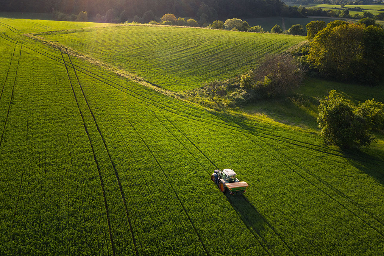 Aerial view on agricultural landscape in spring. A farmer with his machine is driving on a wheat field. Captured with a drone in southern Germany.