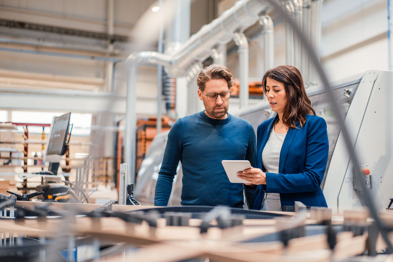 Eine Geschäftsfrau und Geschäftsmann stehen in einer Geschäftshalle und schauen gemeinsam in ein Tablet
