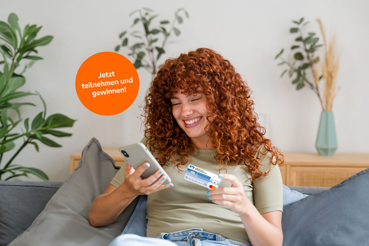 Frau mit lockigen Haaren sitzt auf der Couch und schaut lächelnd auf ihr Handy.