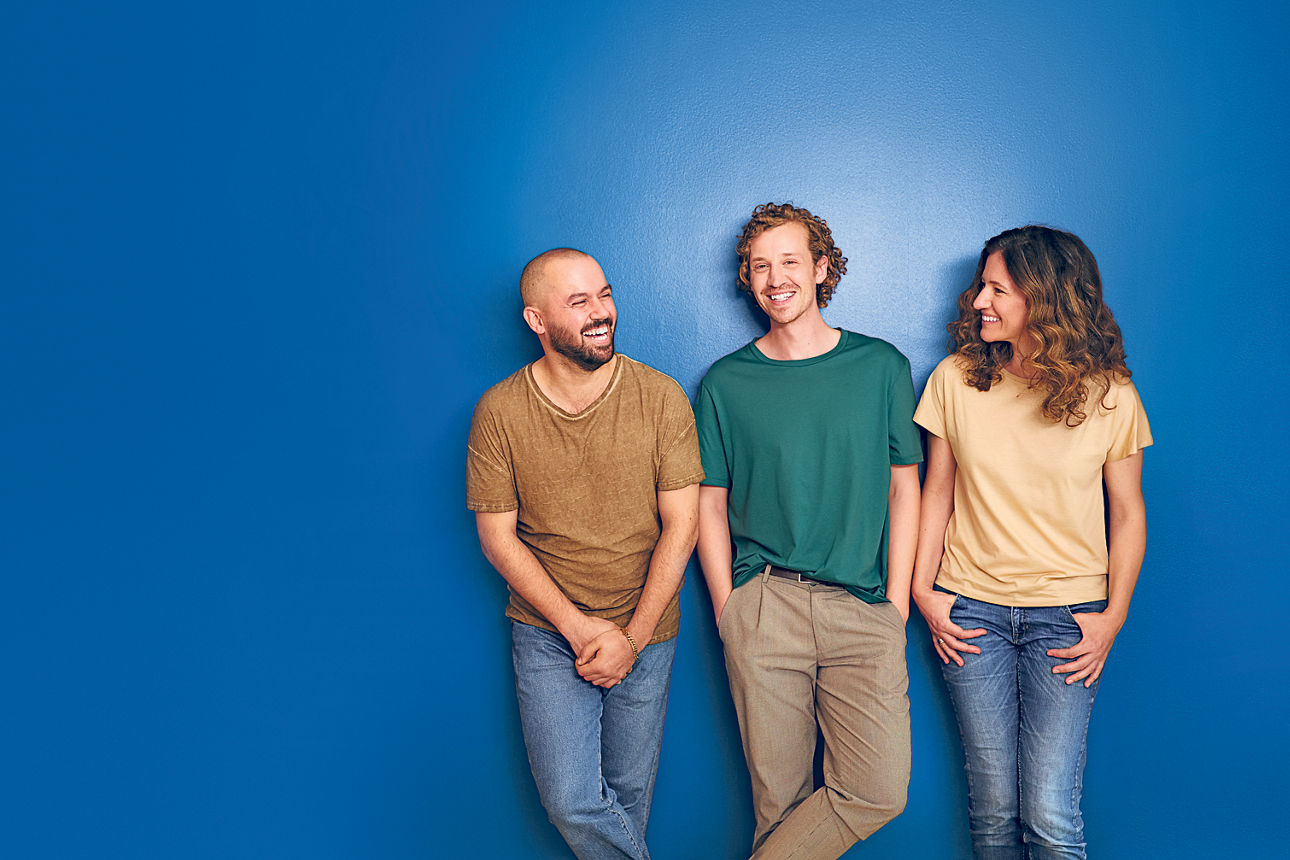 3 Personen die lachend an einer Wand stehen und sich anschauen