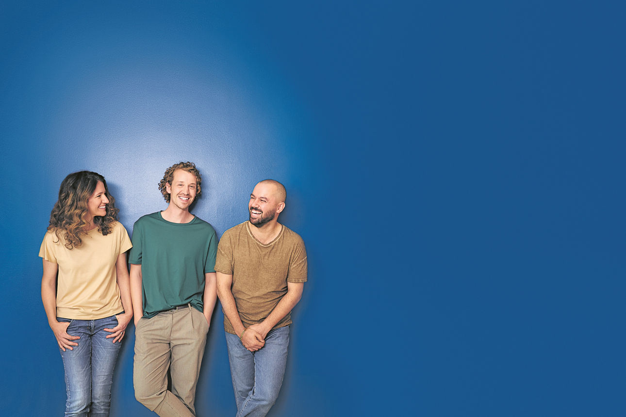 Drei lachende Menschen stehen vor einer blauen Wand mit dem Schriftzug „Wir sind meine Bank.”