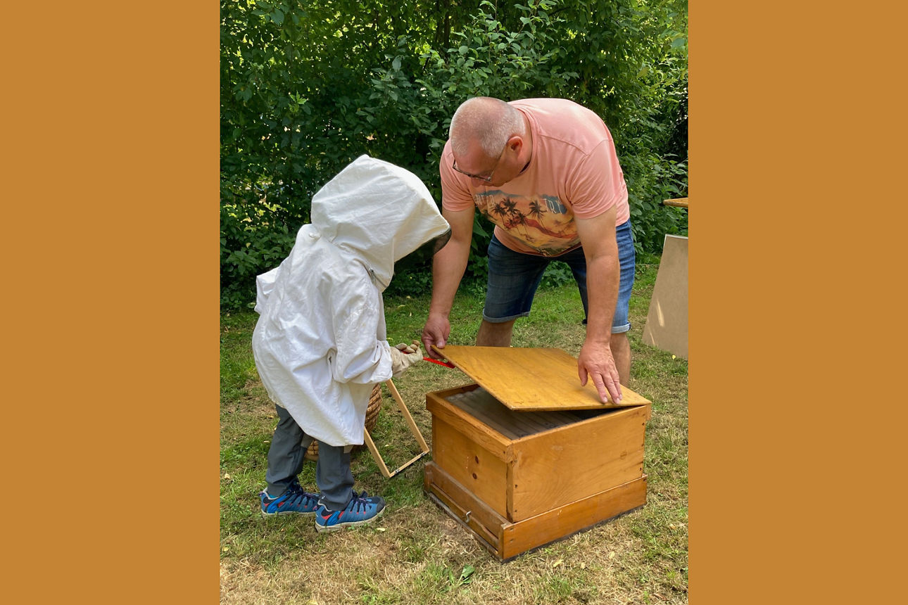 Kind bläst Rauch in einen Bienenstock mit Hilfe des Imkers