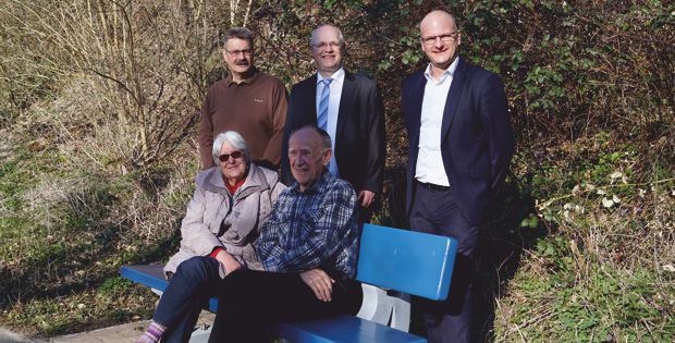 Eine Gruppe von fünf Personen, die auf einer Bank in einem Park stehen und sitzen.