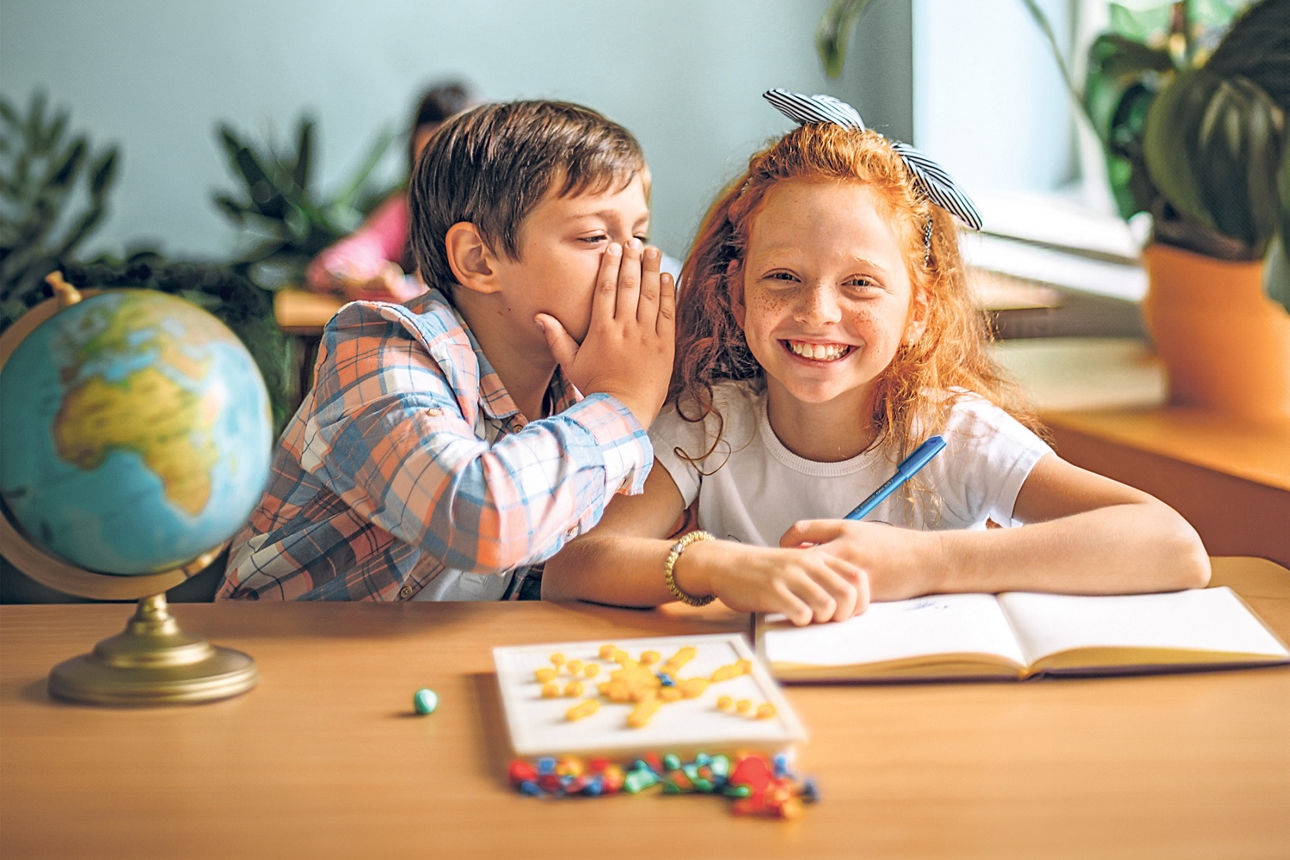 Schüler und Schülerin am Schreibtisch - auf dem Tisch steht ein Globus und liegt ein Buch und ein Würfelspiel.