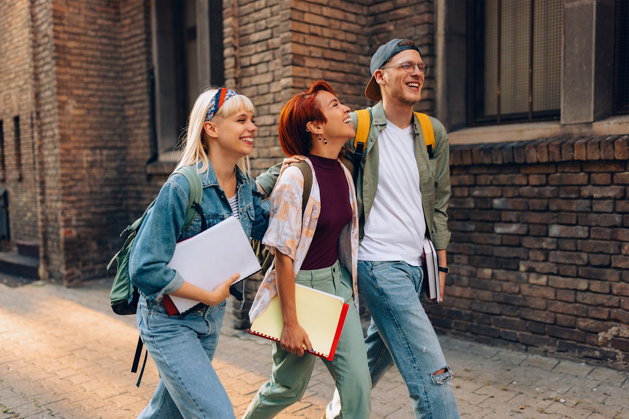 Drei junge Erwachsene laufen an einem Backsteinhaus vorbei.