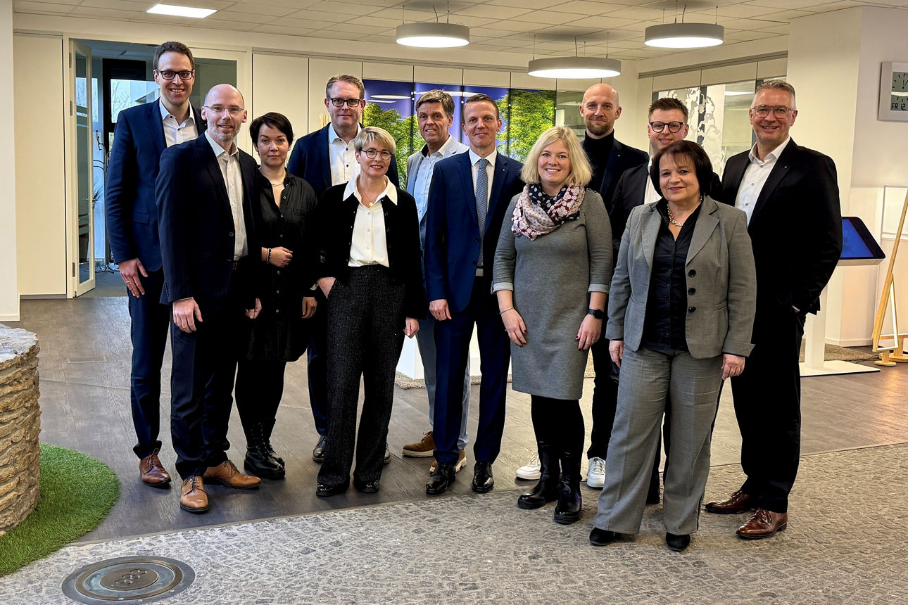 Gruppenporträt von elf Fachleuten, überwiegend in Geschäftskleidung, die sich in einem modernen Bürogebäude versammelt haben.