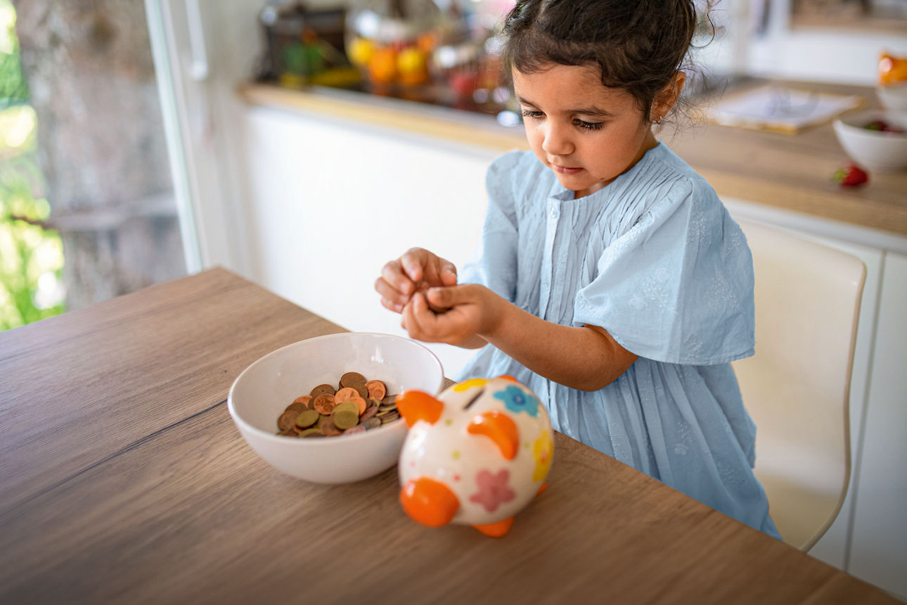 Ein kleines Mädchen zählt Geld von ihrem Sparschwein in eine Schüssel