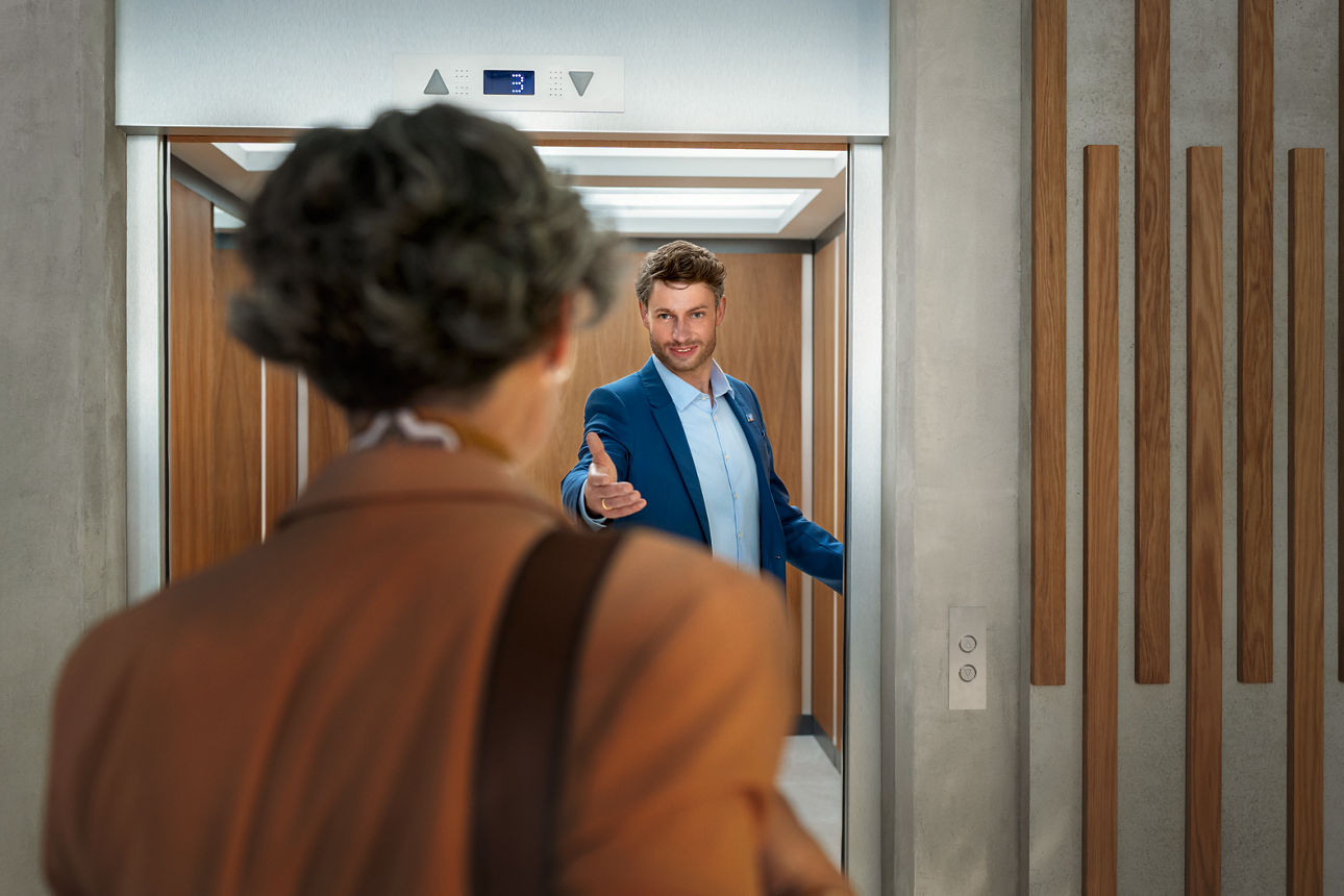 Ein Mann hält einer Frau die Fahrstuhltür offen