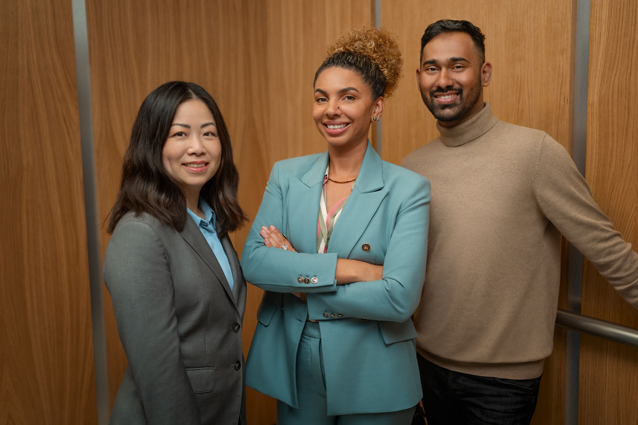 Zwei Frauen und ein Mann stehen in einem Aufzug und lächeln in die Kamera