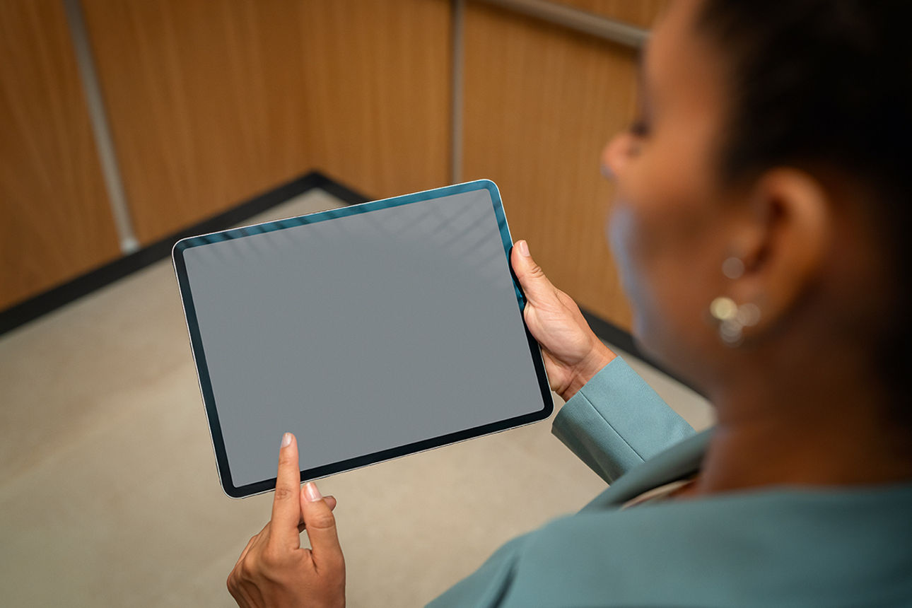 Eine Frau hält ein Tablet in der Hand und zeigt mit dem Finger darauf.