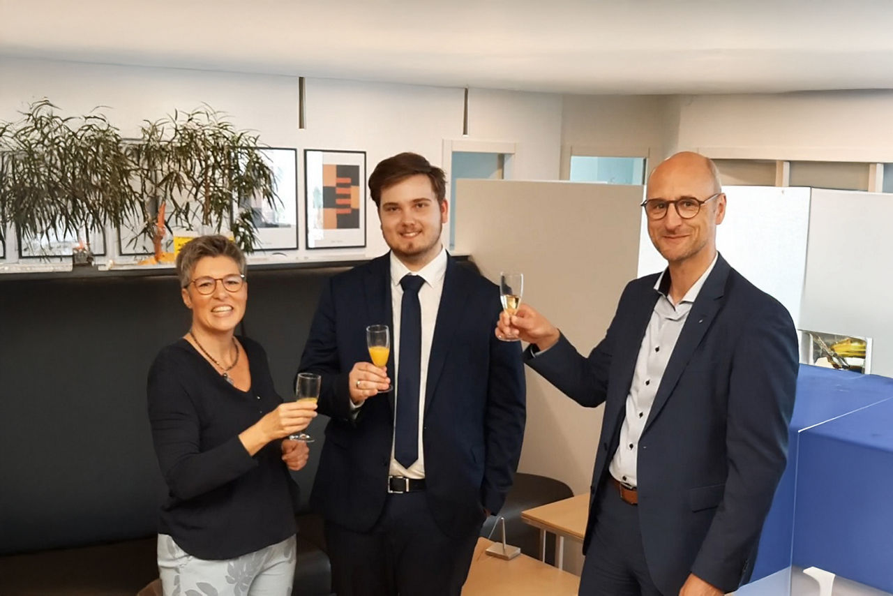 Drei Kollegen feiern ein erfolgreiches Projekt und stoßen in einer modernen Büroumgebung mit einem Glas Sekt an.