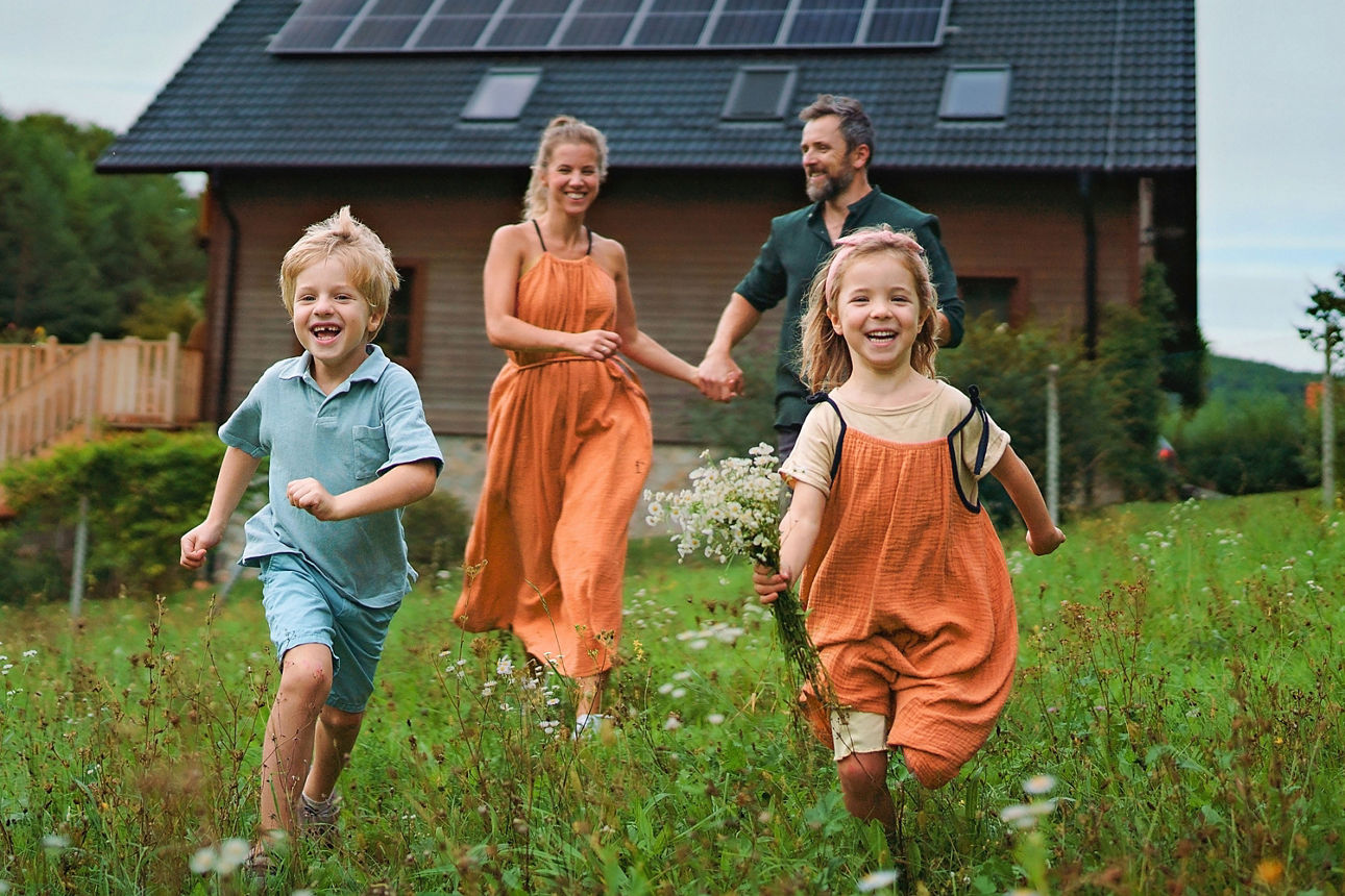 Mann und Frau mit zwei Kindern gehen hinter einem Haus im Garten spazieren.