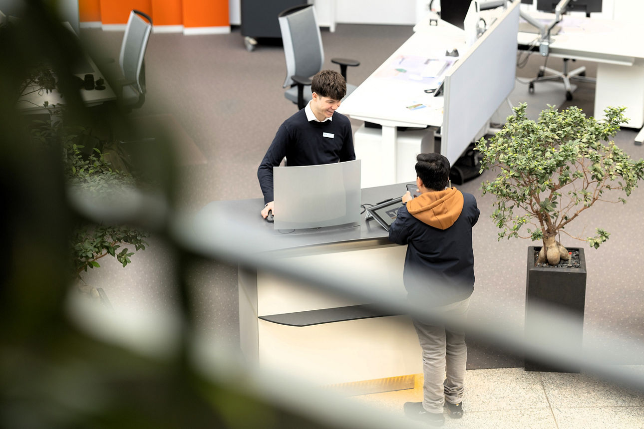 In einer offenen, modernen Schalterhalle steht eine Person an einem Beratungstresen und spricht mit einer anderen Person