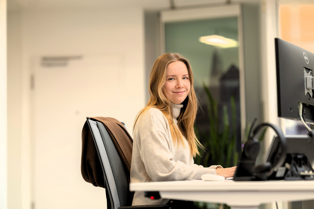 Eine junge weibliche Person sitzt an einem Schreibtisch in einem modernen Büro und arbeitet an einem Computer.