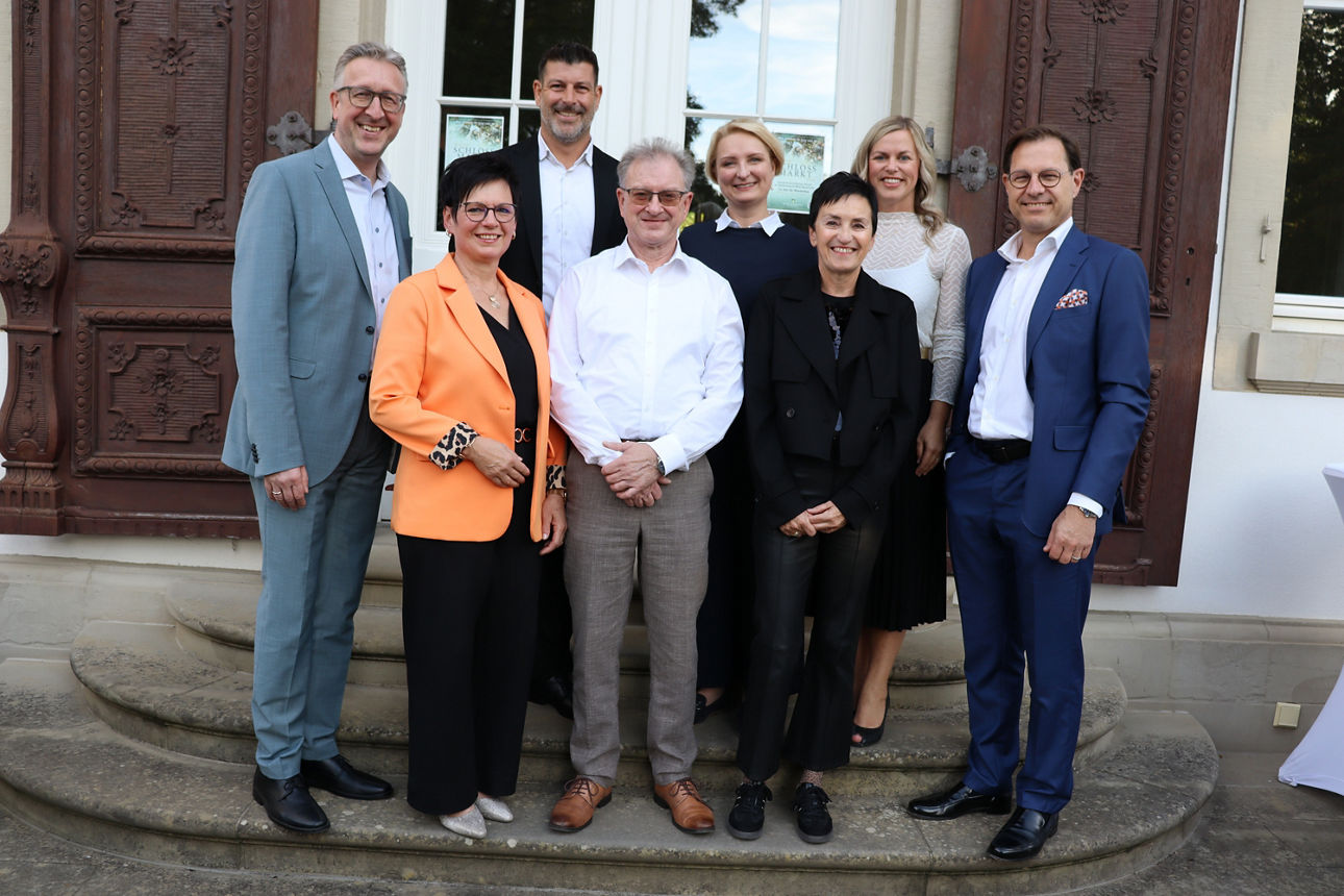 Auf dem Bild sind die Jubilare und Ihre Führungskräfte mit dem Vorstandsvorsitzenden und der Personalleiterin der Bank zu sehen. Sie stehen im Freien auf einer Treppe und lächeln in die Kamera.