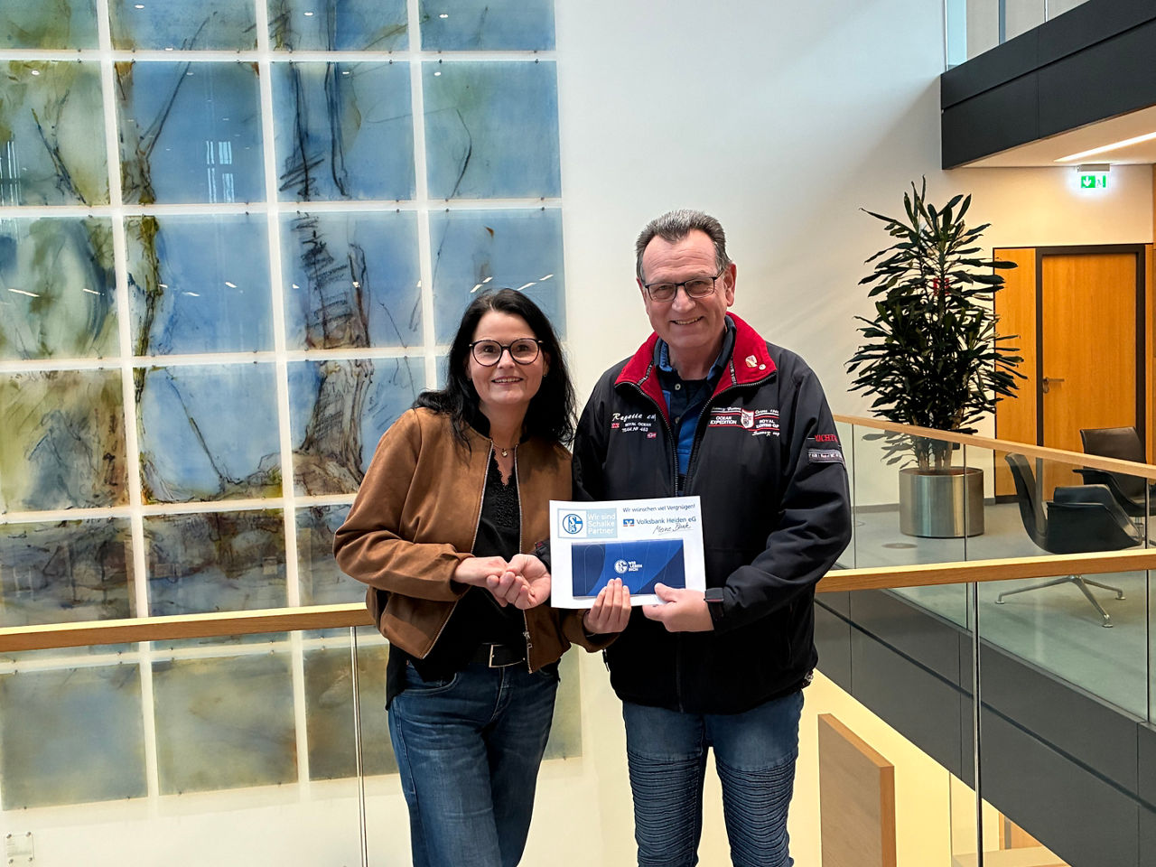 Ein Mann und eine Frau halten stolz gemeinsam eine Urkunde in einem professionellen Büro