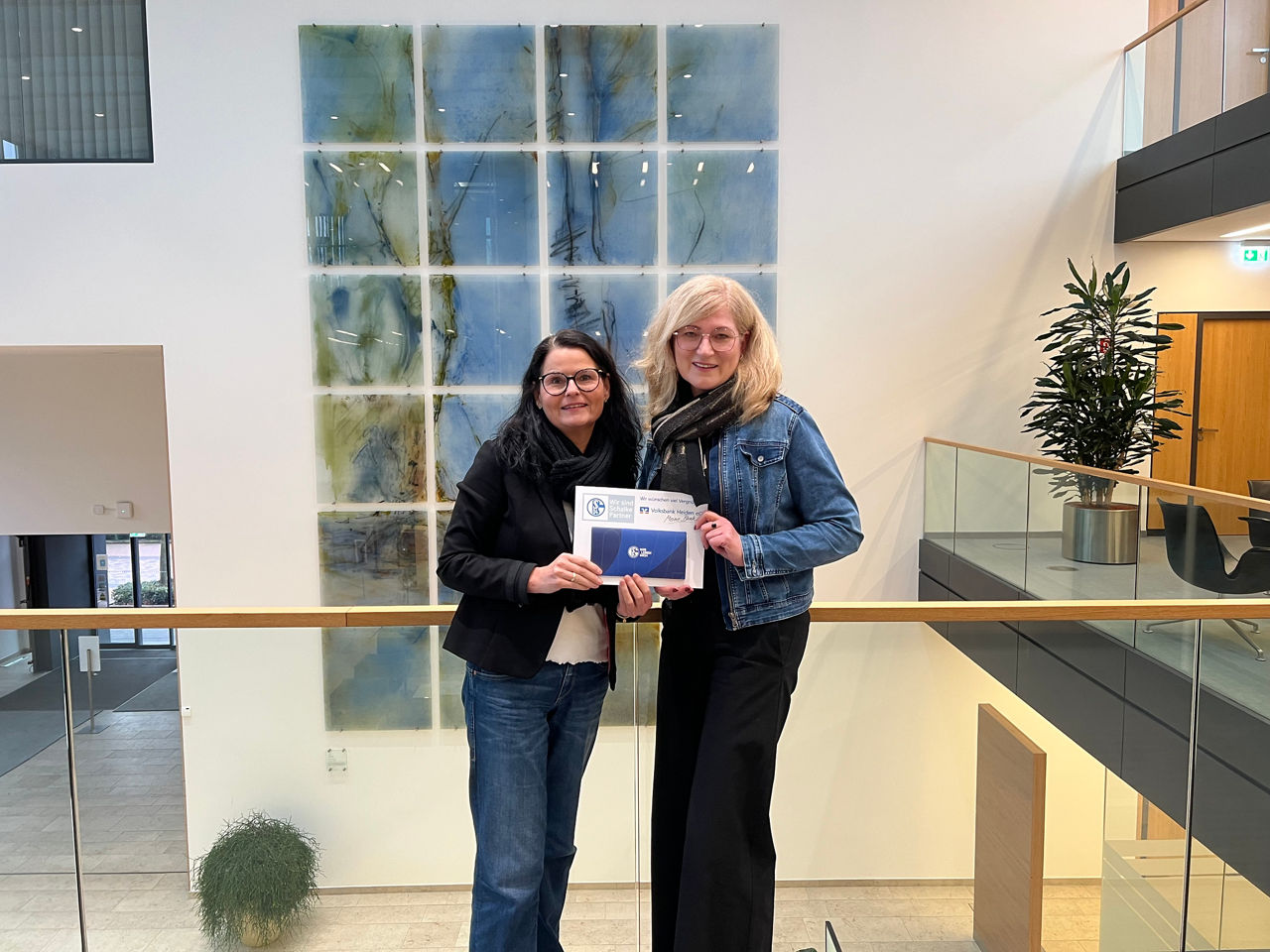 Zwei Frauen stehen zusammen vor einem großen Fenster, wobei natürliches Licht ihre Umgebung erhellt