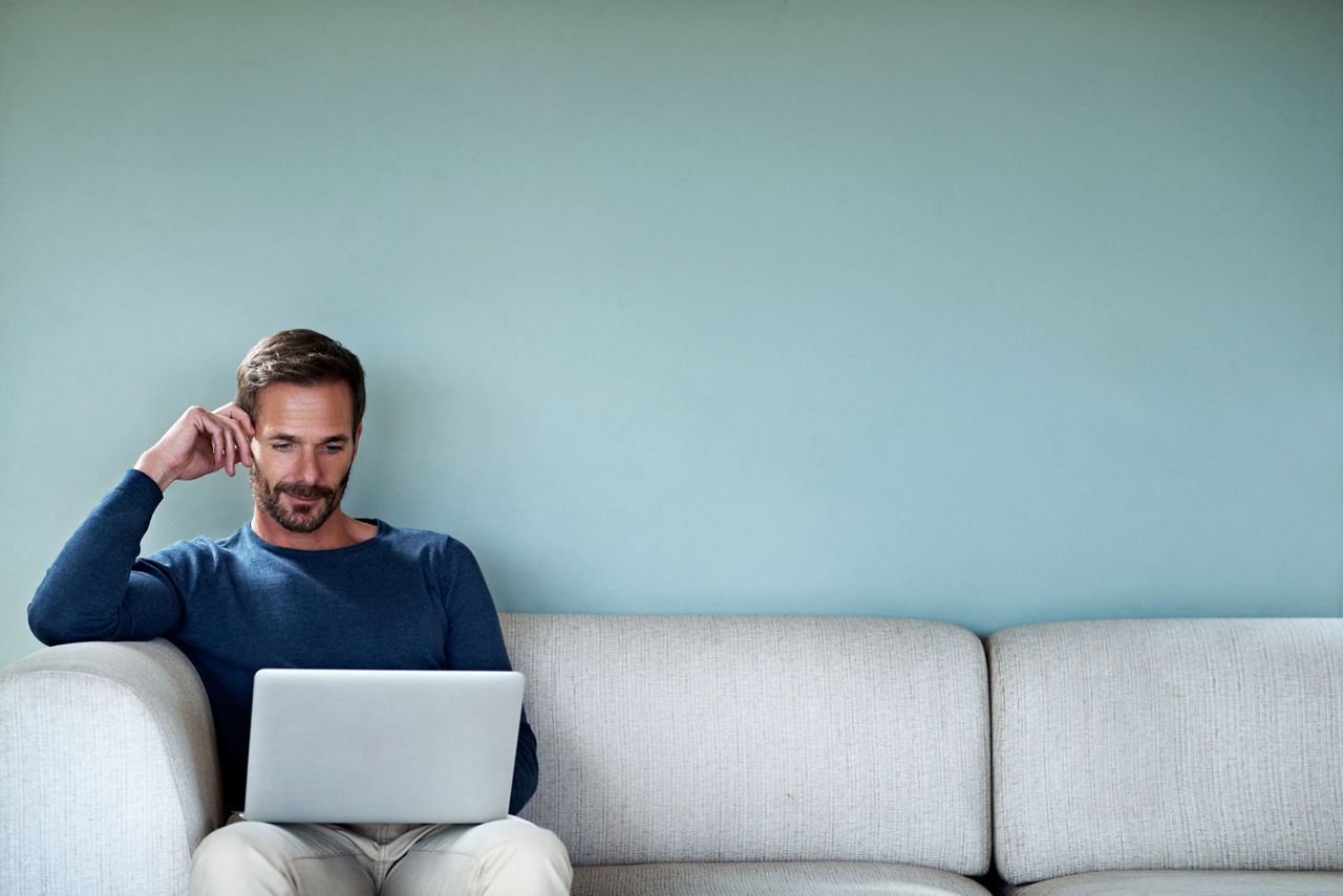 Cropped shot of a handsome man using his laptop while sitting on the living room sofa