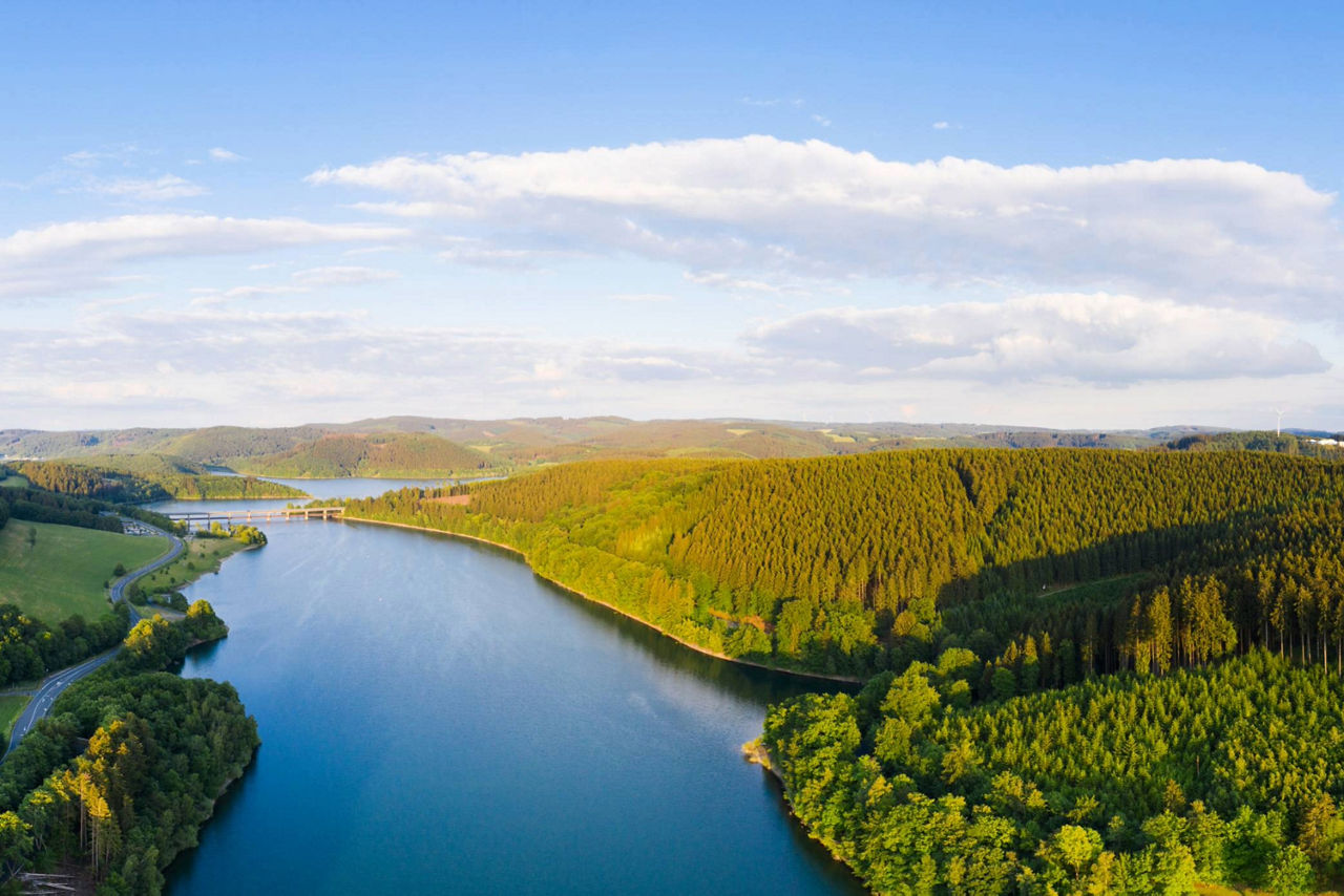 Der Biggesee im Sauerland liegt in einer grünen Landschaft mit vielen Hügeln umgeben von Hügeln.