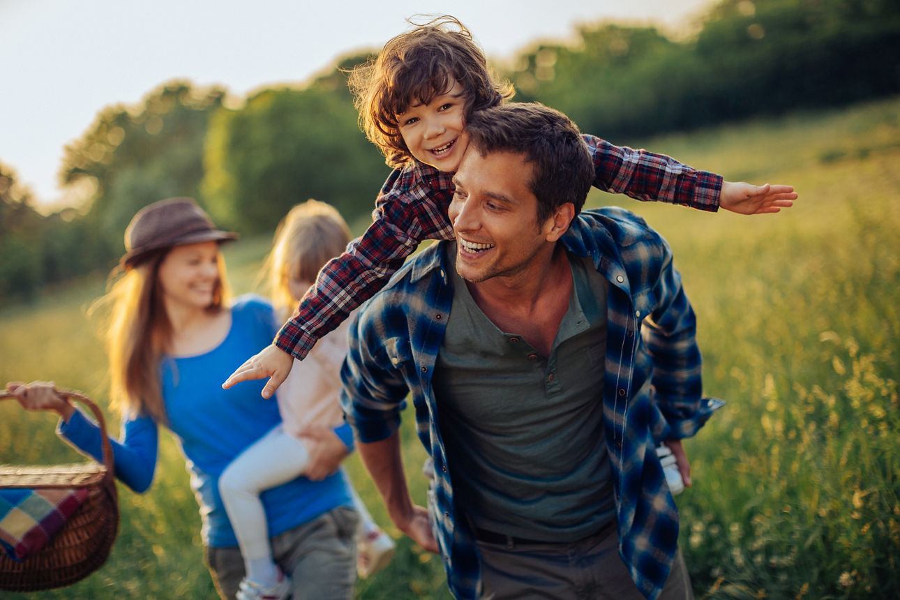 Picture of a young family going for a picnic, walking together threw high grass with the sun in their back.