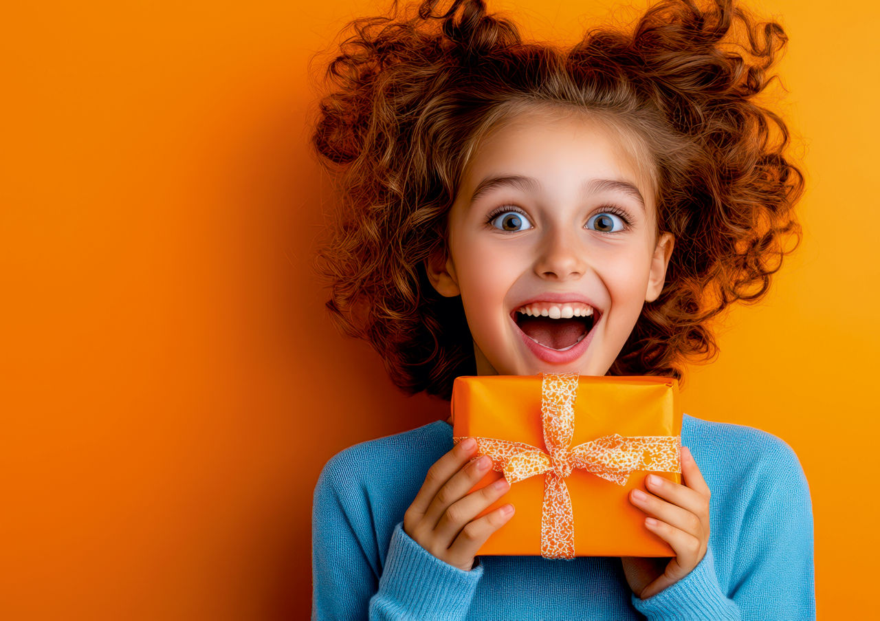 Ein Kind hat ein orangenes Geschenk in der Hand und steht vor einem orangenen Hintergrund. 