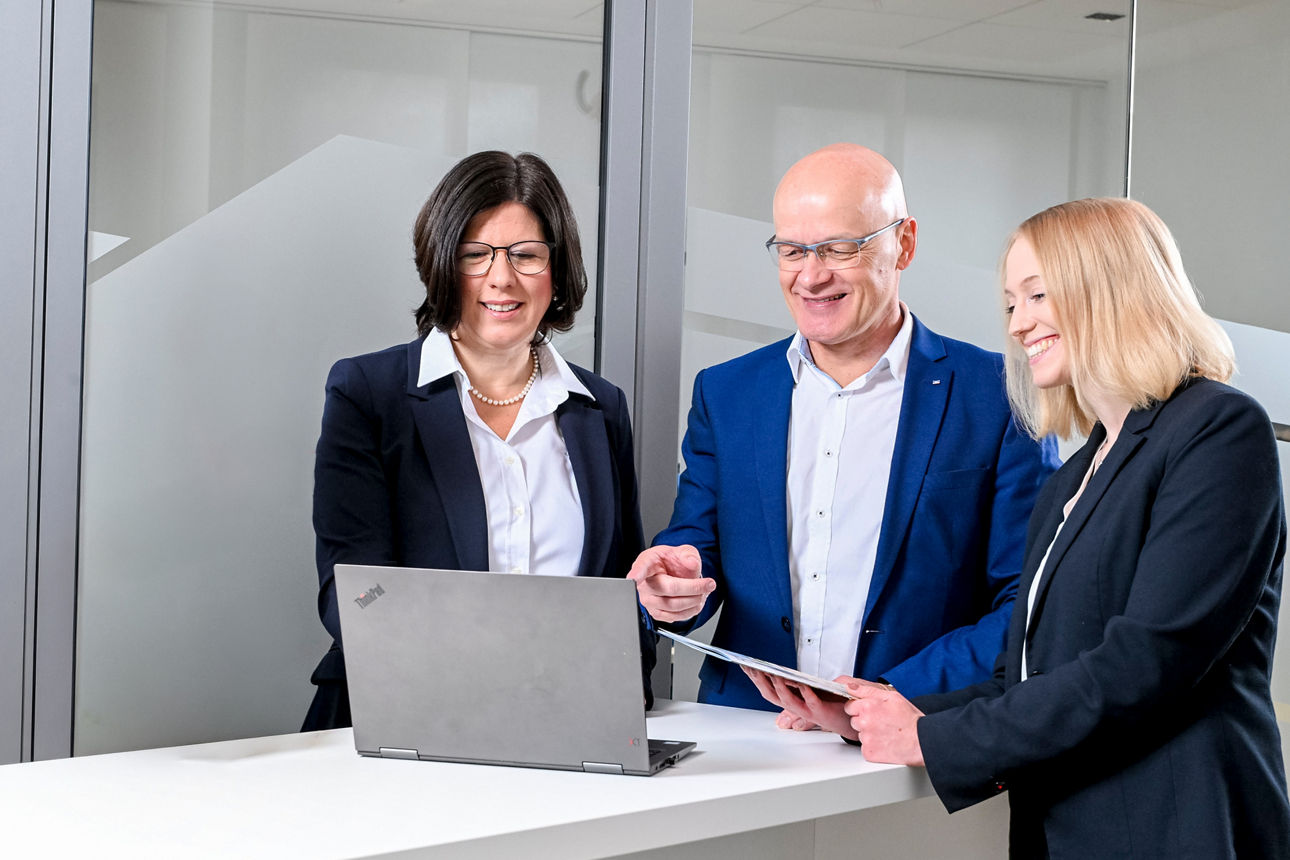 Frau Wördehoff, Herr Heppe & Frau Hölscher (von li.) stehen vor einem Notebook im Büro 