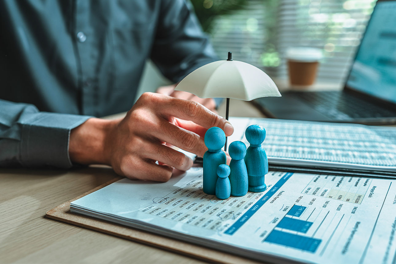 4 Holzfiguren stehen unter einem Regenschirm