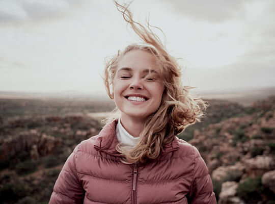 Eine junge Frau lächelt in die Kamera, ihre Haare wehen im Wind