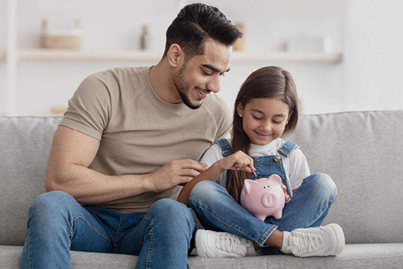 Ein Vater befüllt mit seinem Kind ein Sparschwein