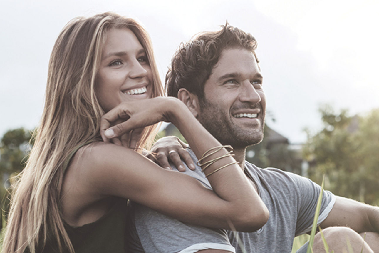 Ein Paar sitzt auf der Wiese und lächelt.