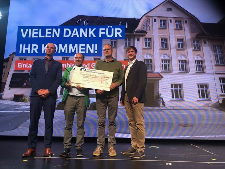 Vier Männer auf einer Bühne präsentieren einen Scheck