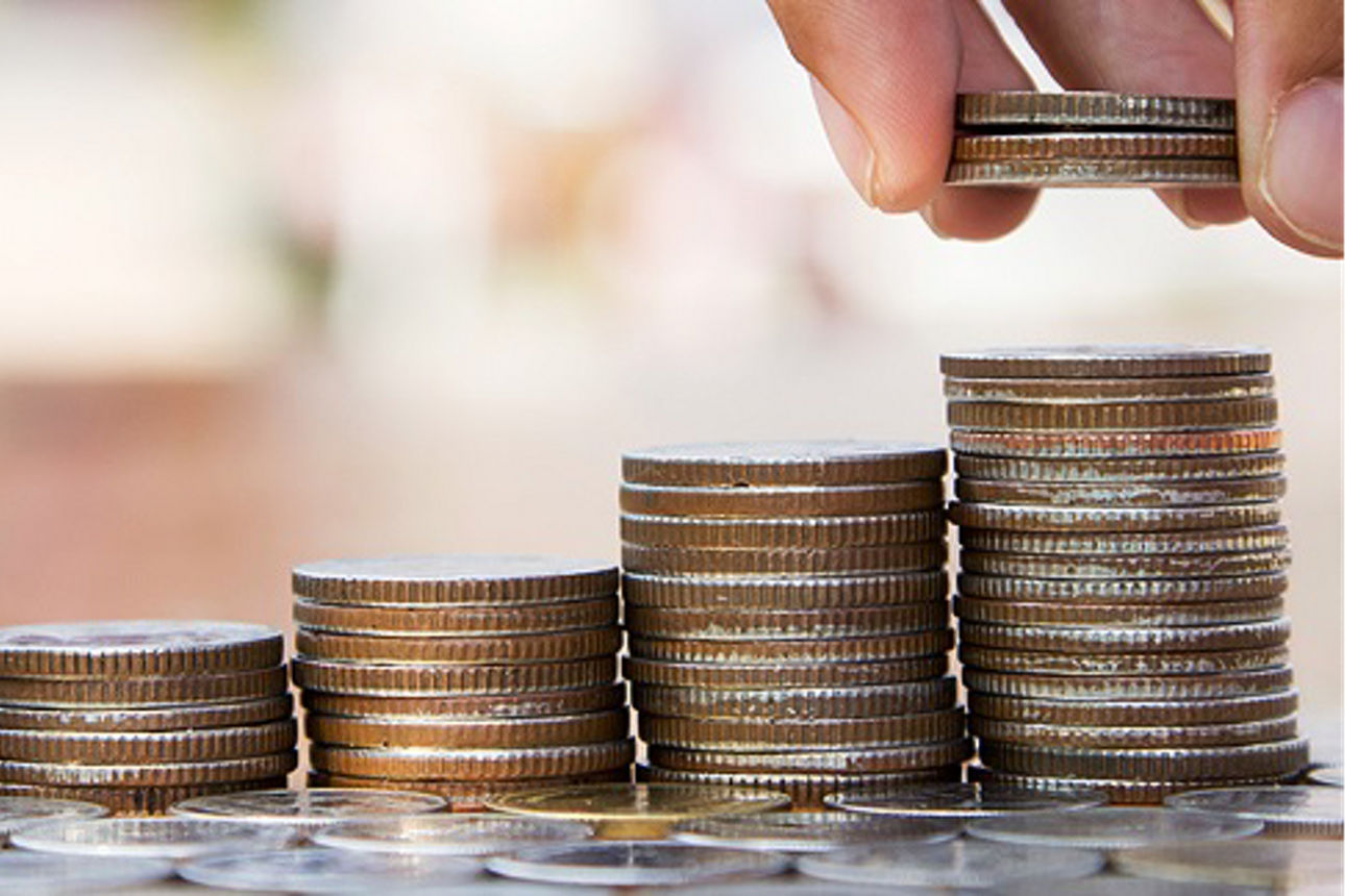 Eine Person legt vorsichtig Münzen auf einen wachsenden Stapel von Münzen