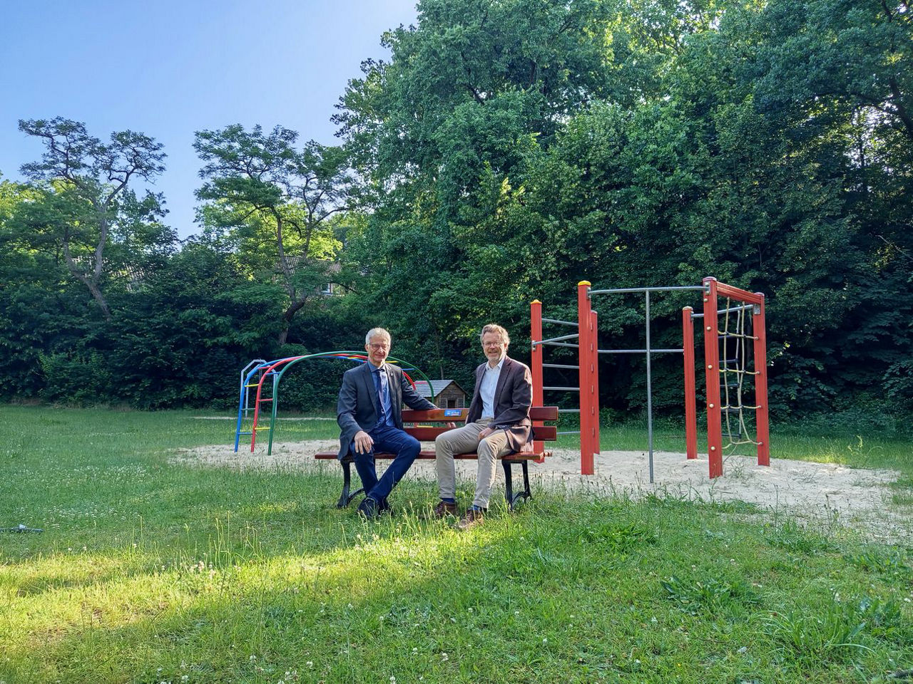 Zwei Herren sitzen auf der gespendeten Bank auf einer Wiese. 