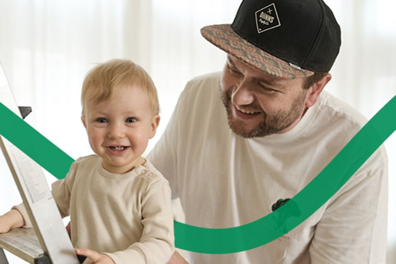 Während der Vater das Kind festhält, steht es auf der Leiter im Wohnzimmer. 