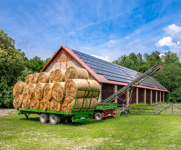 Stall mit Solaranlage auf dem Dach, davor ein Wagen mit Heuballen