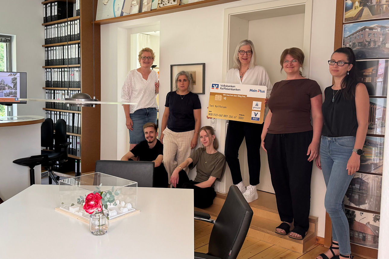 Ein Team von Fachleuten steht gemeinsam in einem Büro und hält eine große Werbekreditkarte in den Händen.