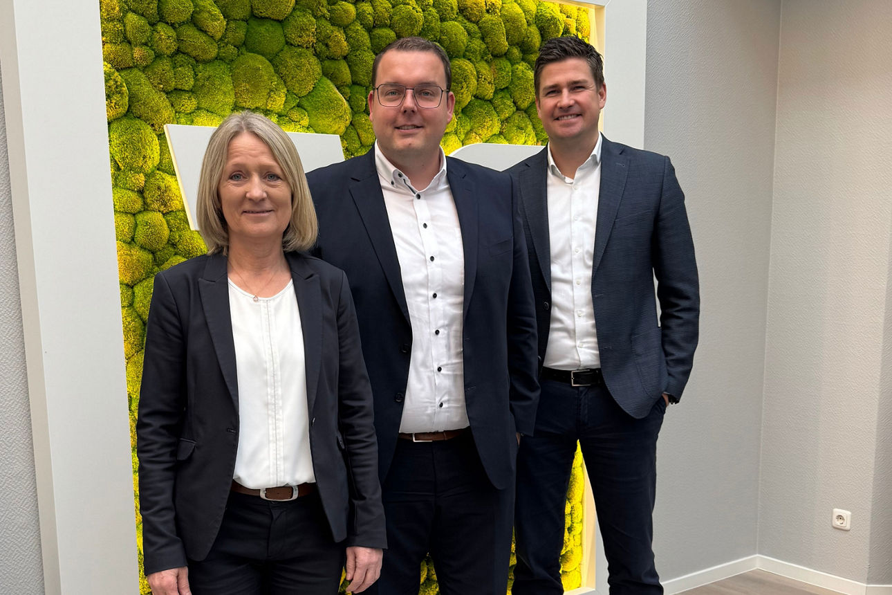 Drei Bankmitarbeitende in Businesskleidung vor einer grünen Wand